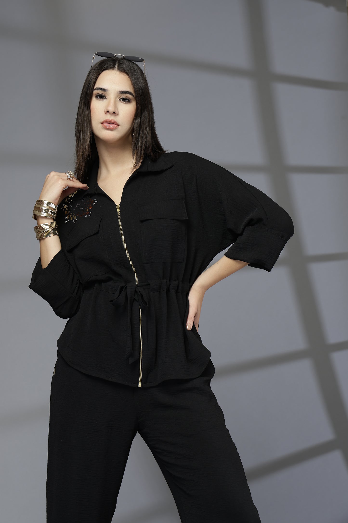 Woman wearing a black outfit with gold accents against a gray background