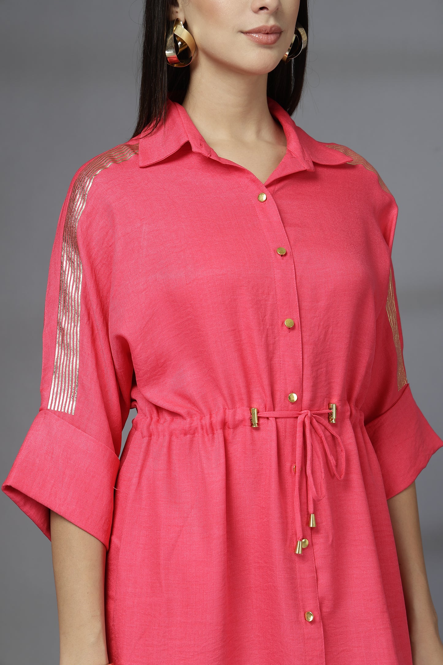 Woman wearing a pink dress with sheer sleeves against a gray background