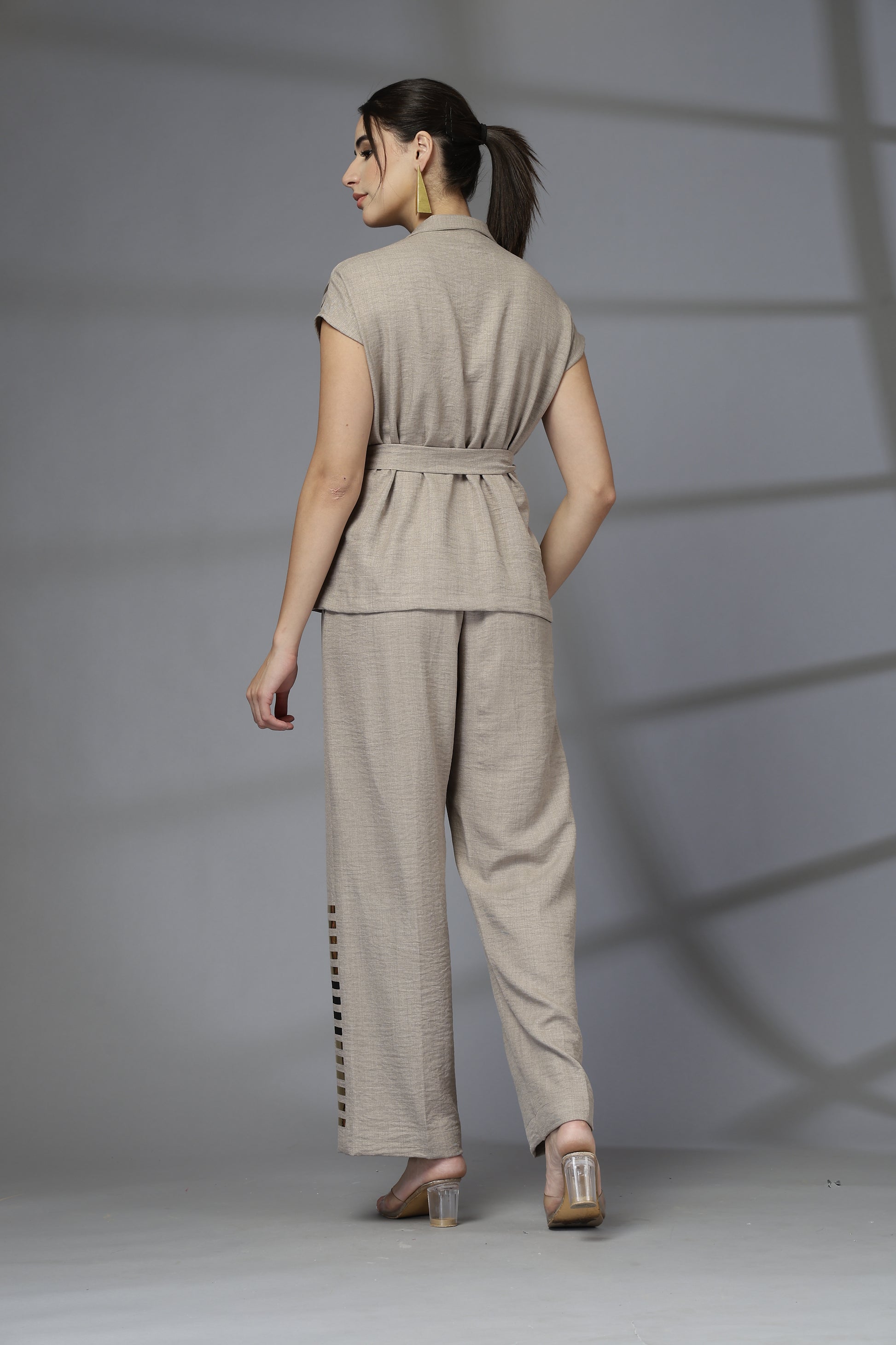 Woman wearing a beige outfit with a belt against a gray background