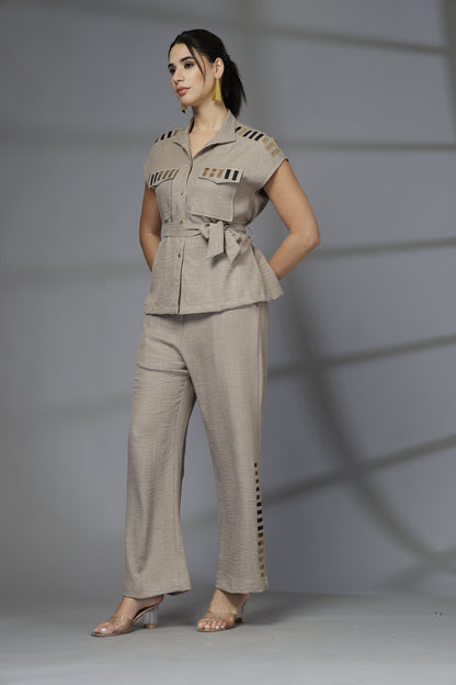 Woman wearing a beige outfit with a belt against a gray background