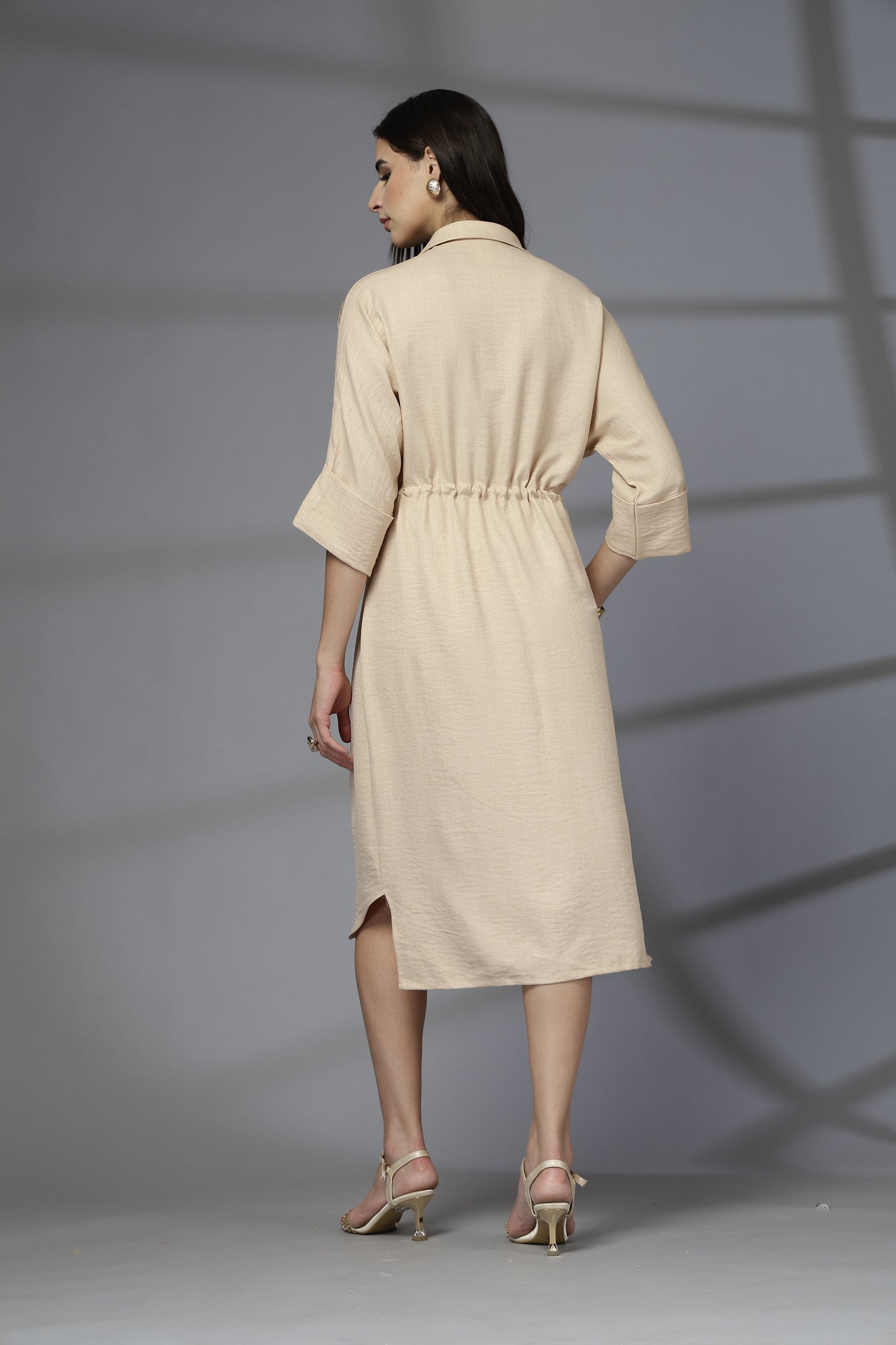 Woman wearing a beige dress standing against a gray background