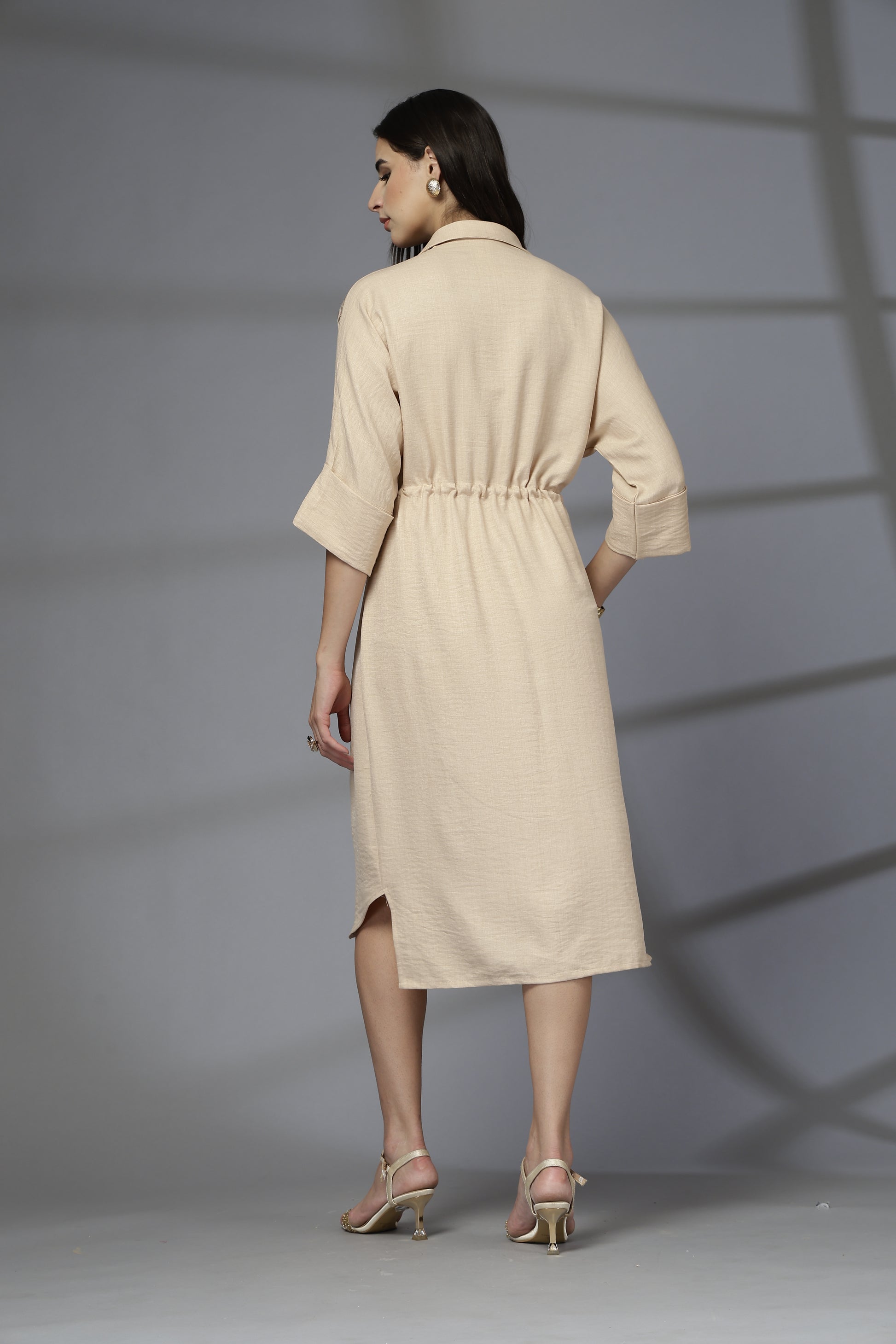 Woman wearing a beige dress standing against a gray background