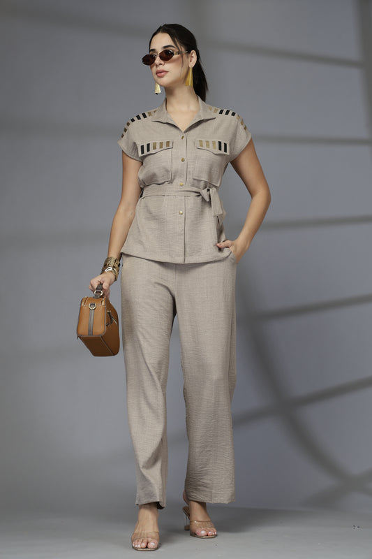 Woman in a beige outfit holding a brown handbag against a gray background