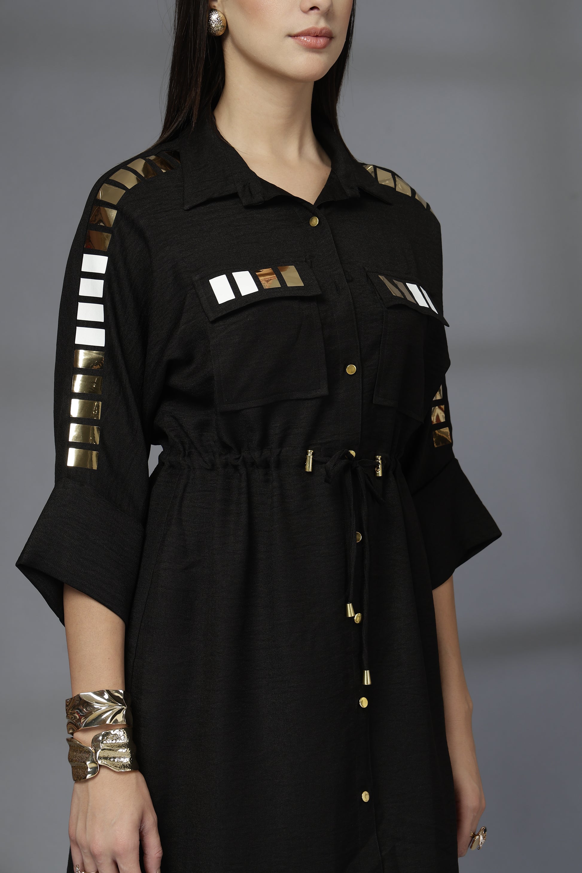 Black dress with gold accents worn by a model on a gray background