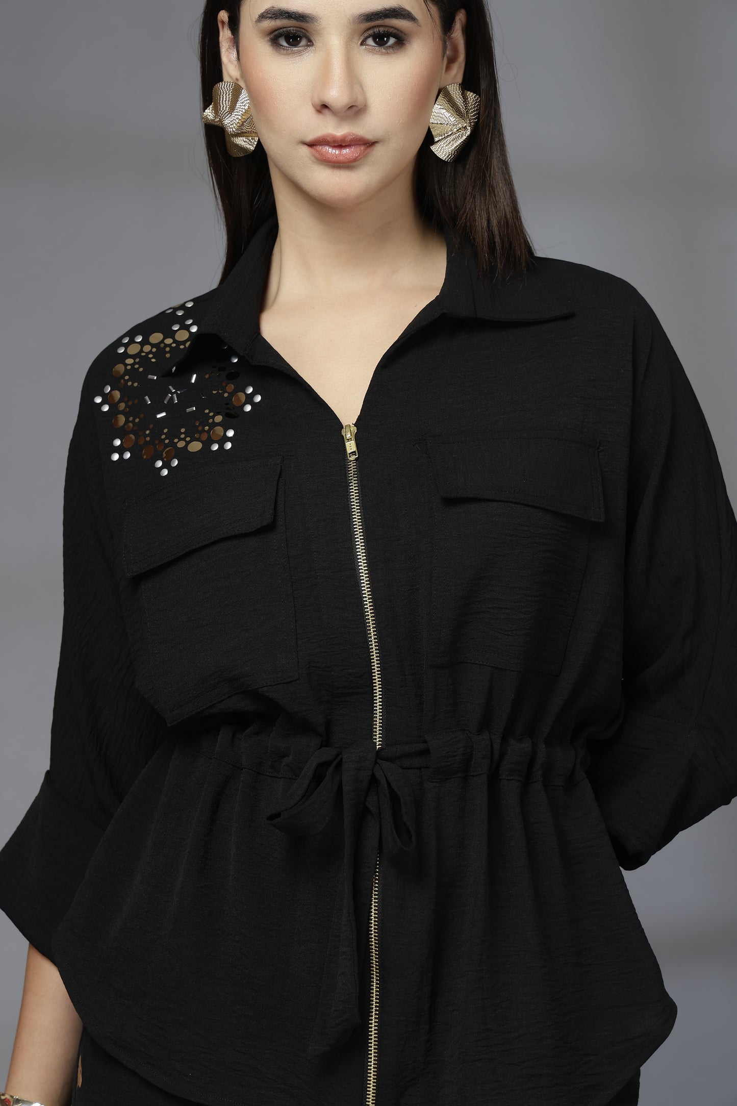 Woman wearing a black outfit with decorative elements on a gray background