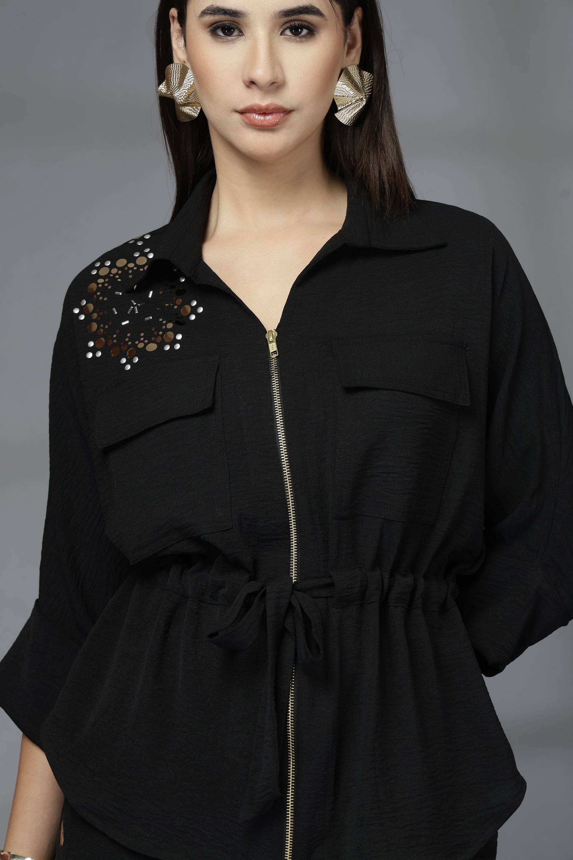 Woman wearing a black outfit with decorative elements on a gray background