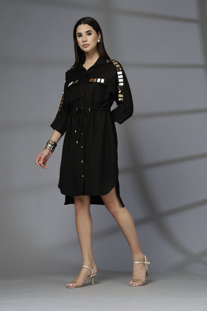 Woman in a black dress with gold accents posing against a gray background