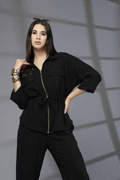 Woman wearing a black outfit with gold accents against a gray background