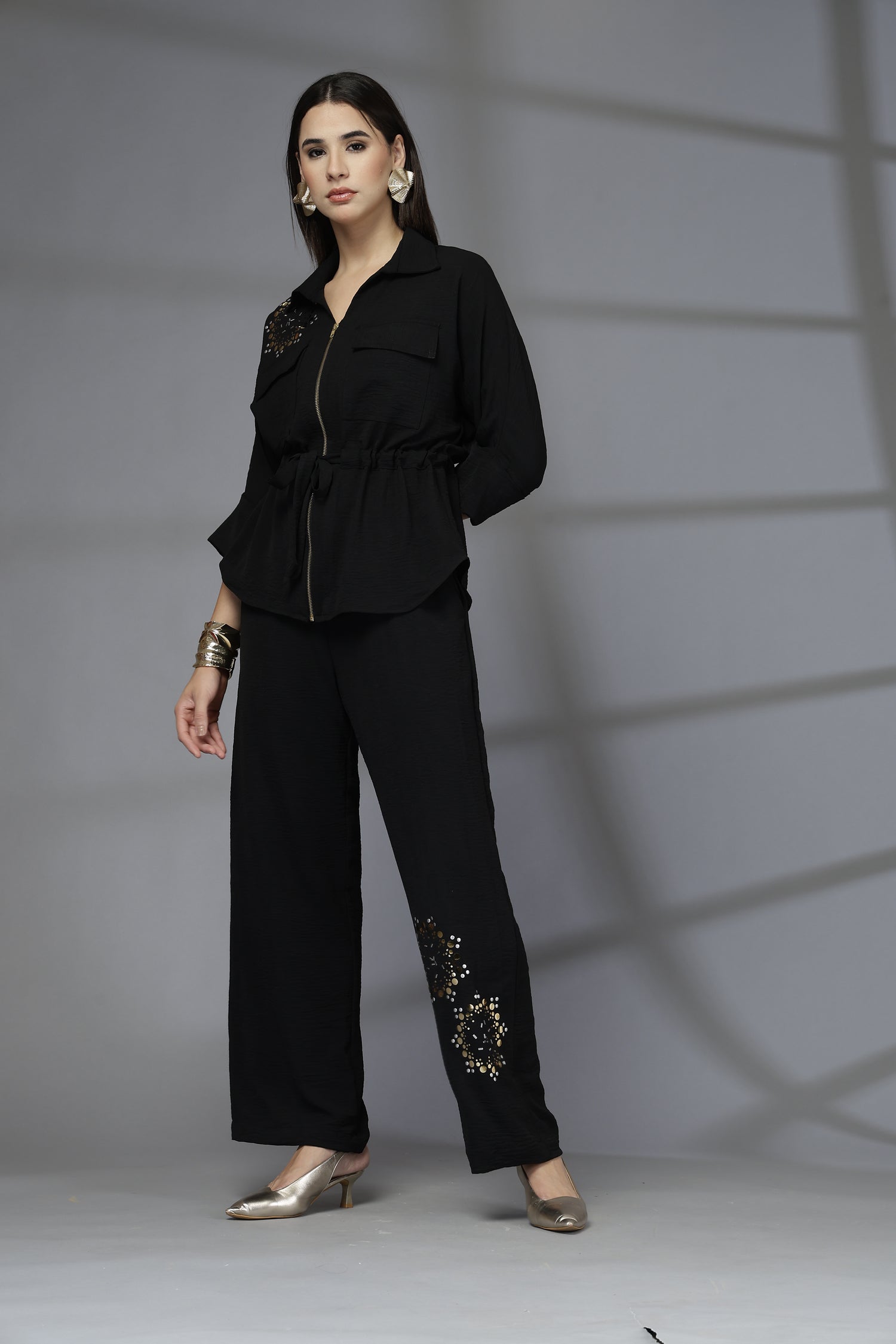 Person wearing a black outfit with decorative elements on a plain background