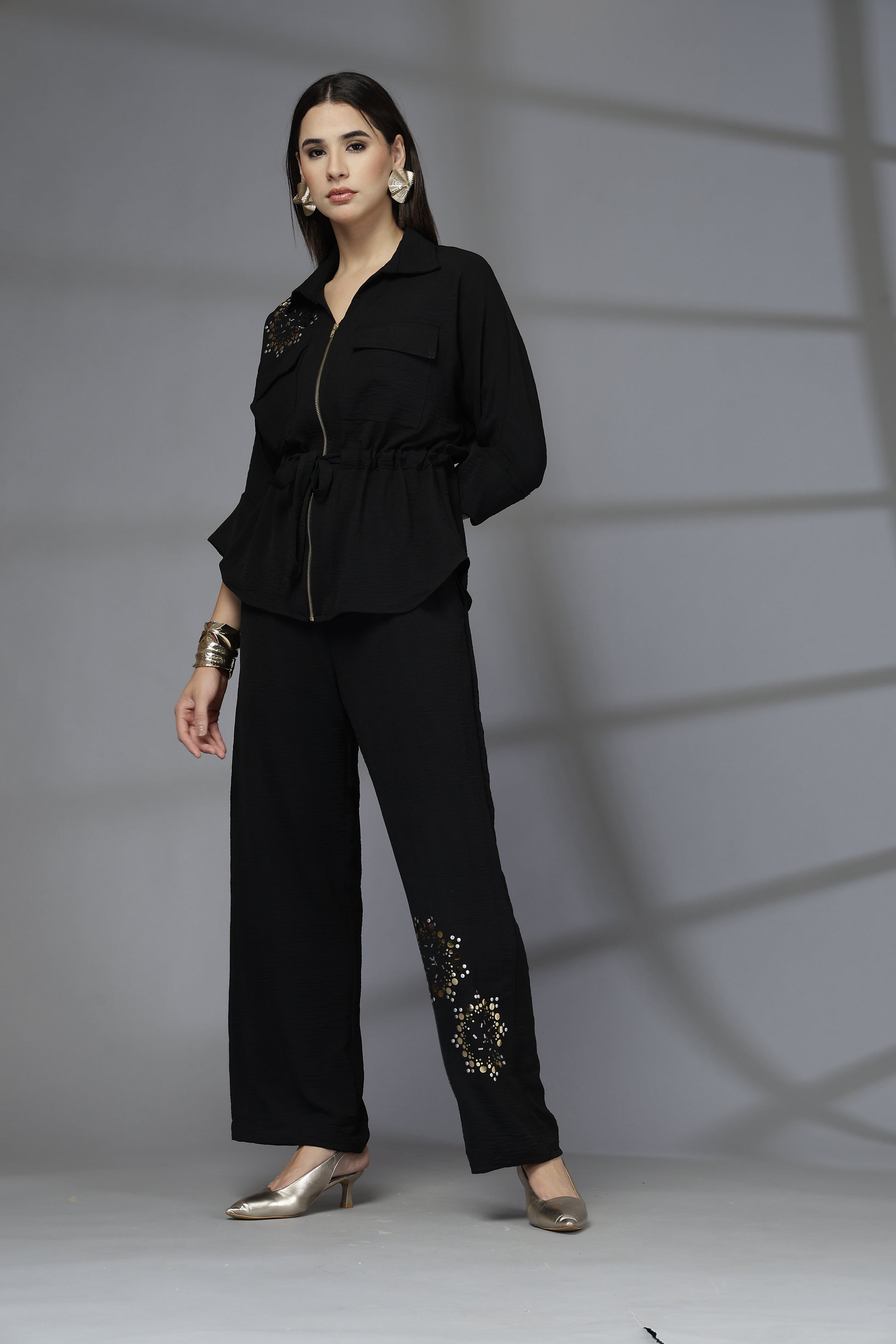 Person wearing a black outfit with decorative elements on a plain background