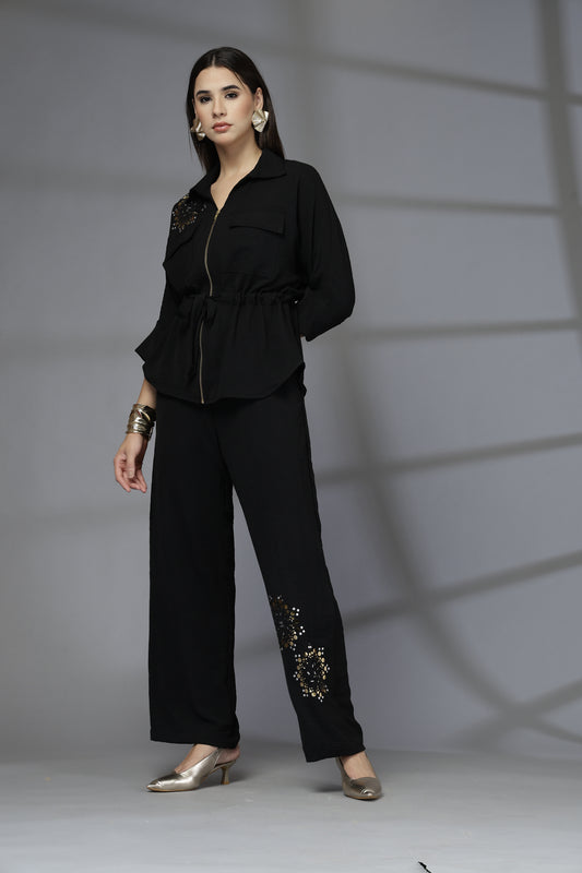 Person wearing a black outfit with decorative elements on a plain background