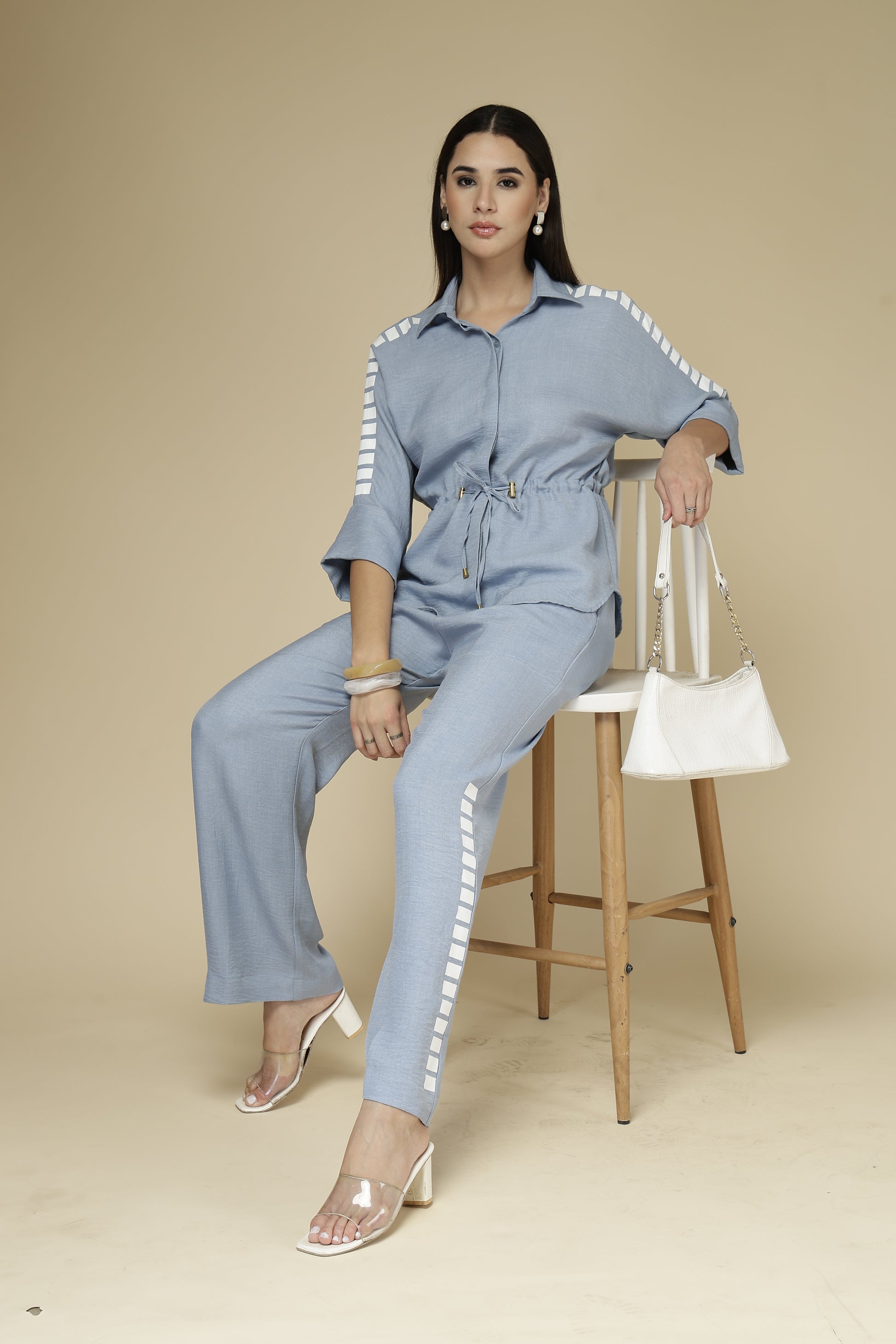 Woman in a light blue outfit sitting on a stool against a beige background