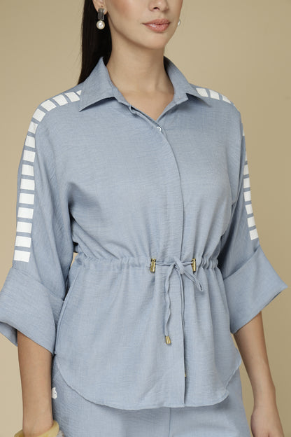 Woman wearing a light blue shirt with white stripes on sleeves against a beige background