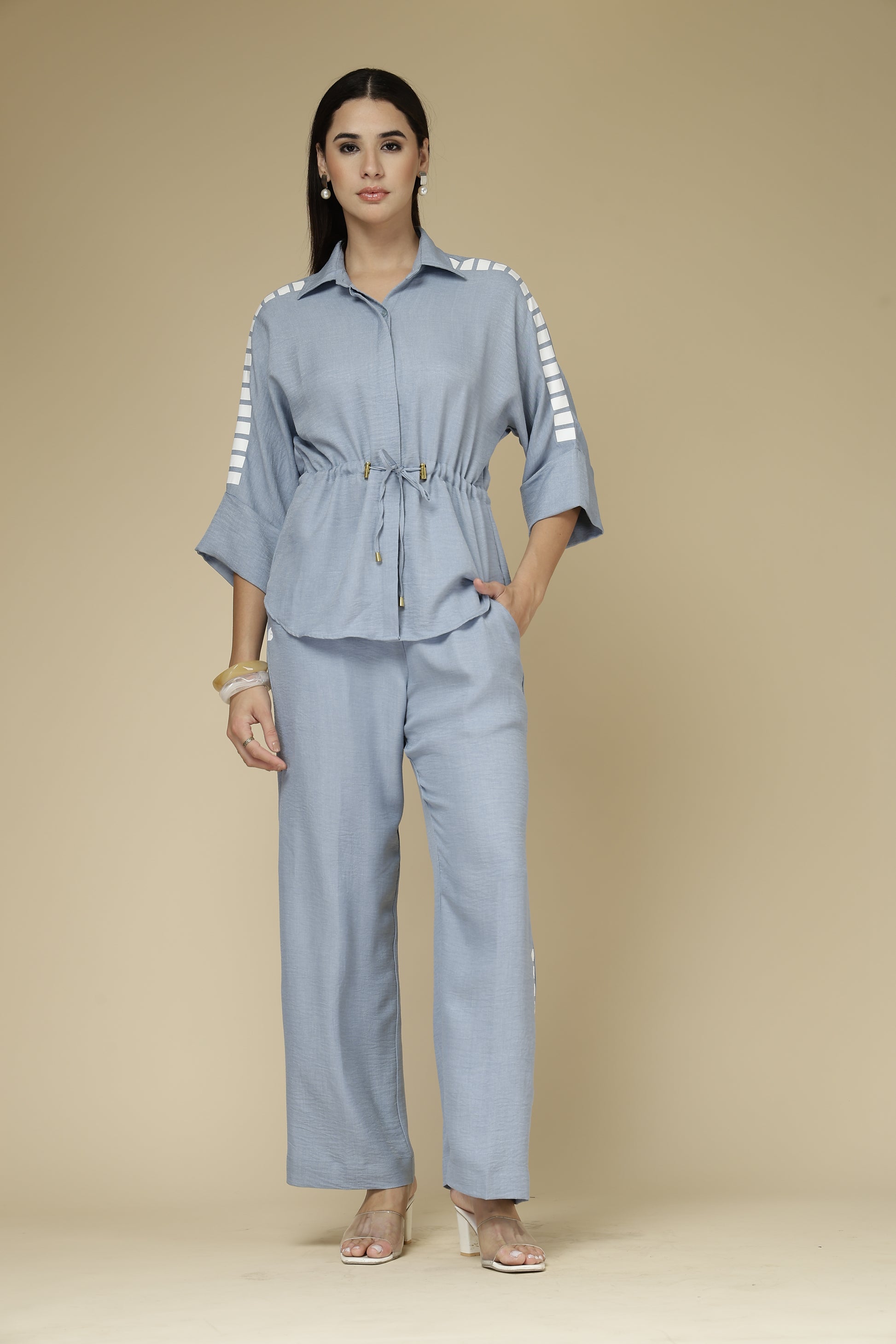 Woman wearing a light blue outfit with a matching jacket and pants on a beige background