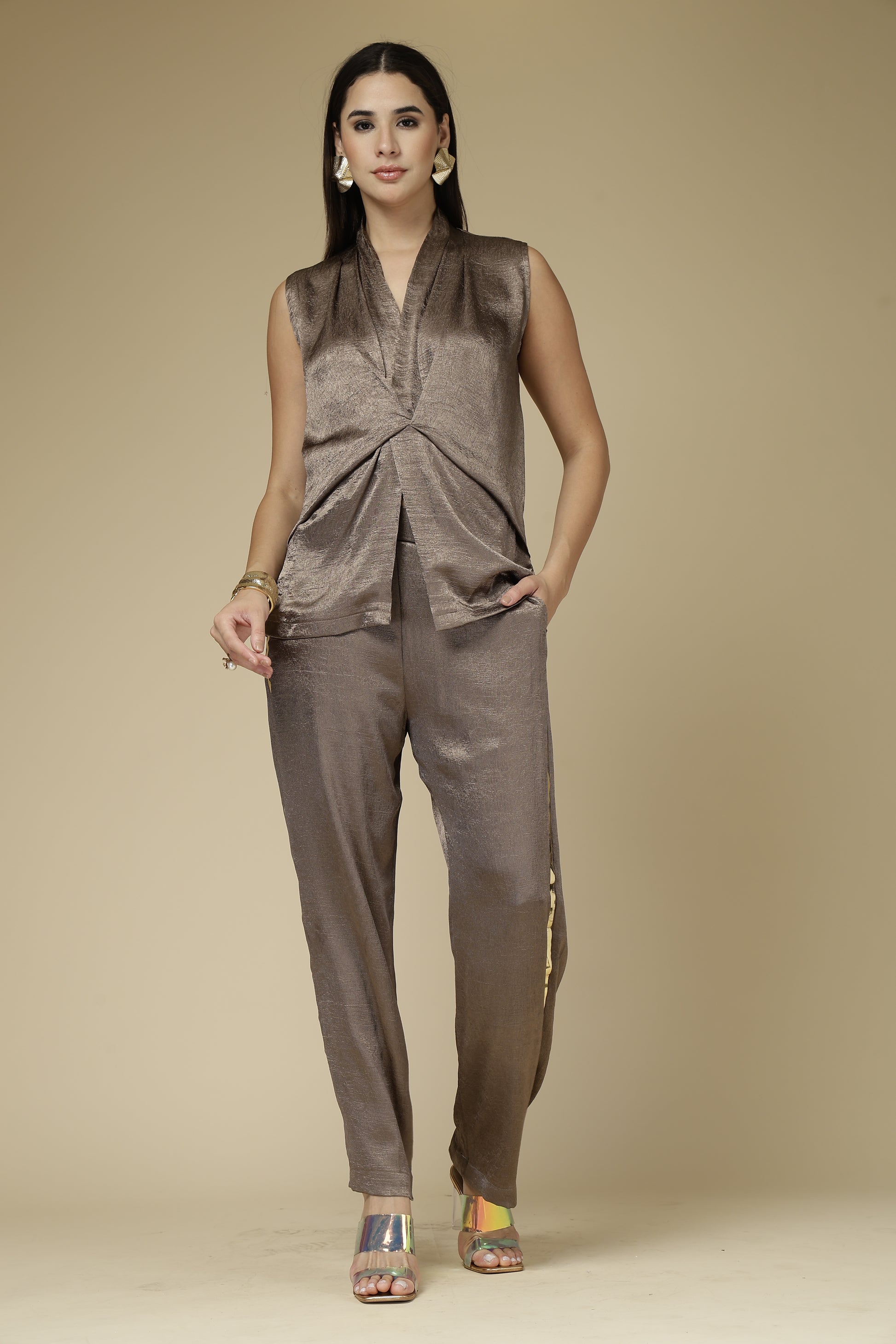 Woman wearing a brown sleeveless top and pants against a beige background