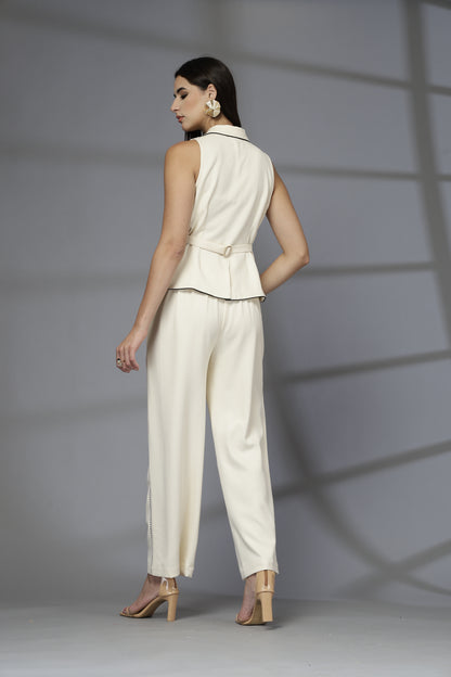 Woman wearing a cream sleeveless top and pants against a gray background