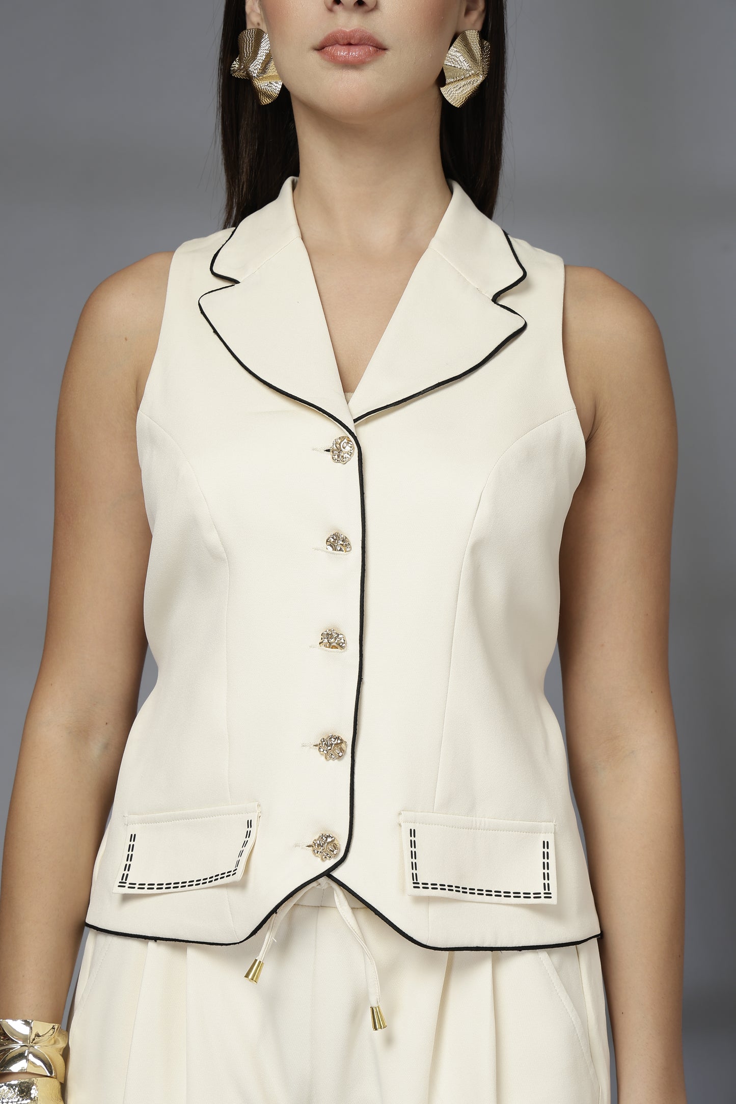 Woman wearing a white sleeveless blazer with black trim on a gray background