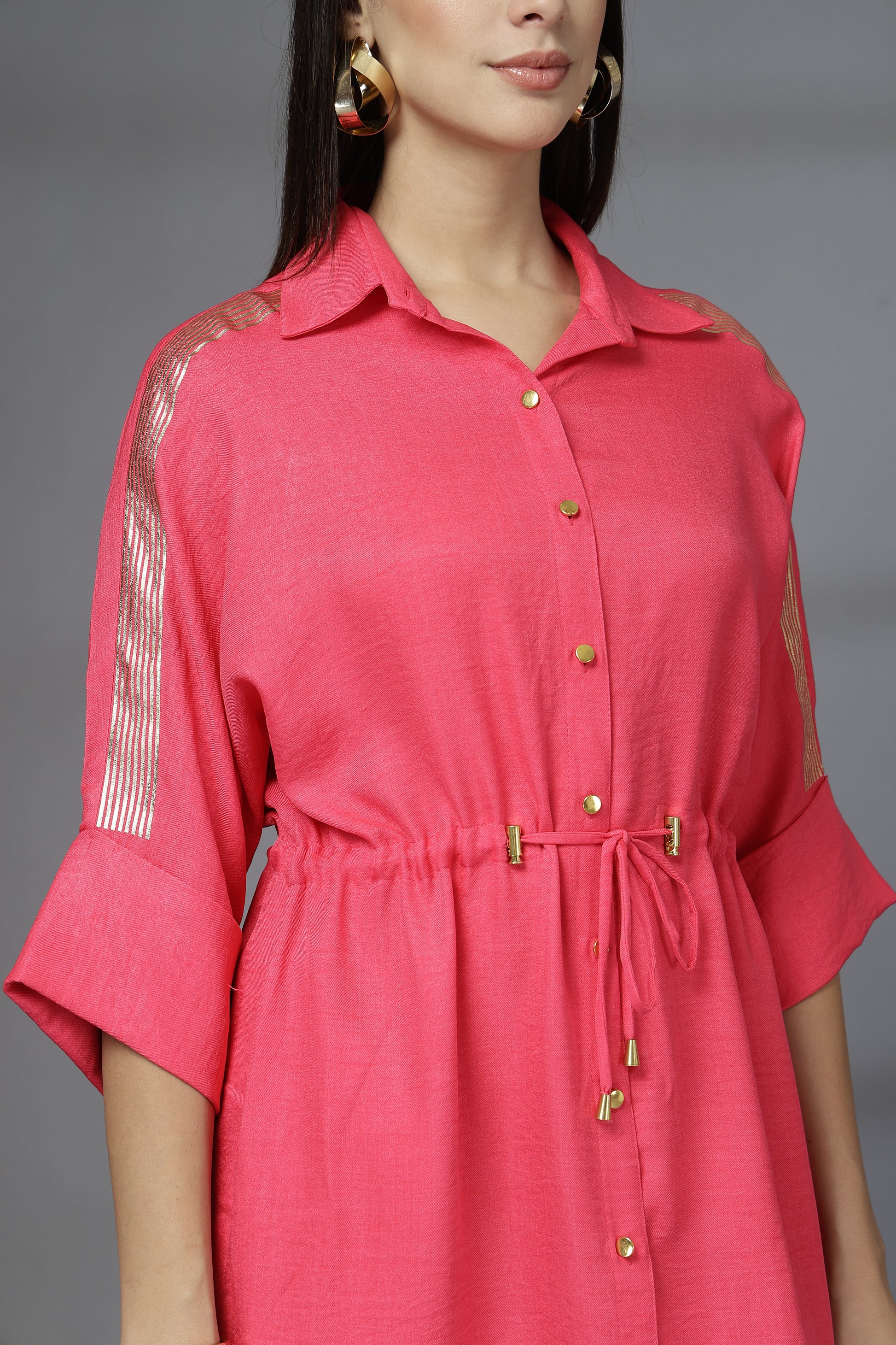 Woman wearing a pink dress with sheer sleeves against a gray background