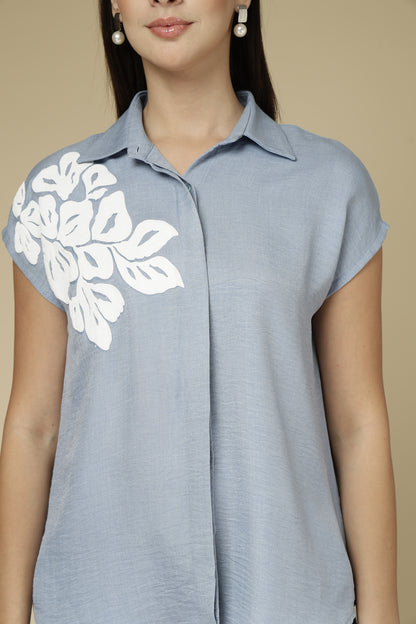 Light blue shirt with white floral embroidery on a beige background