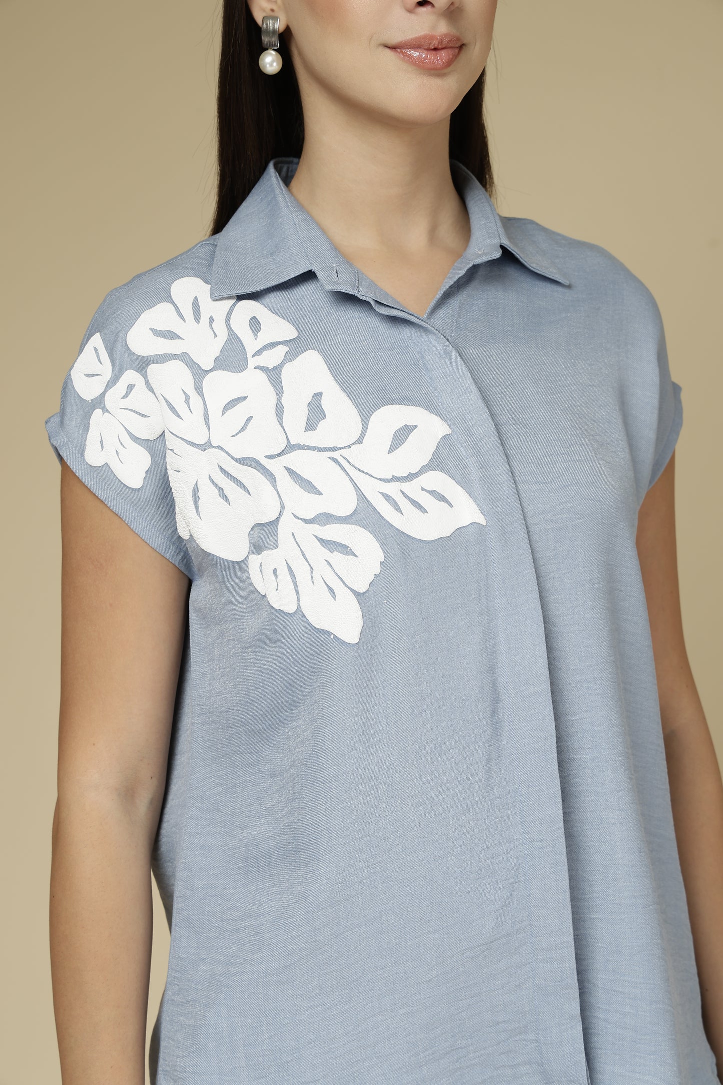 Woman wearing a light blue sleeveless top with white floral patterns on a beige background