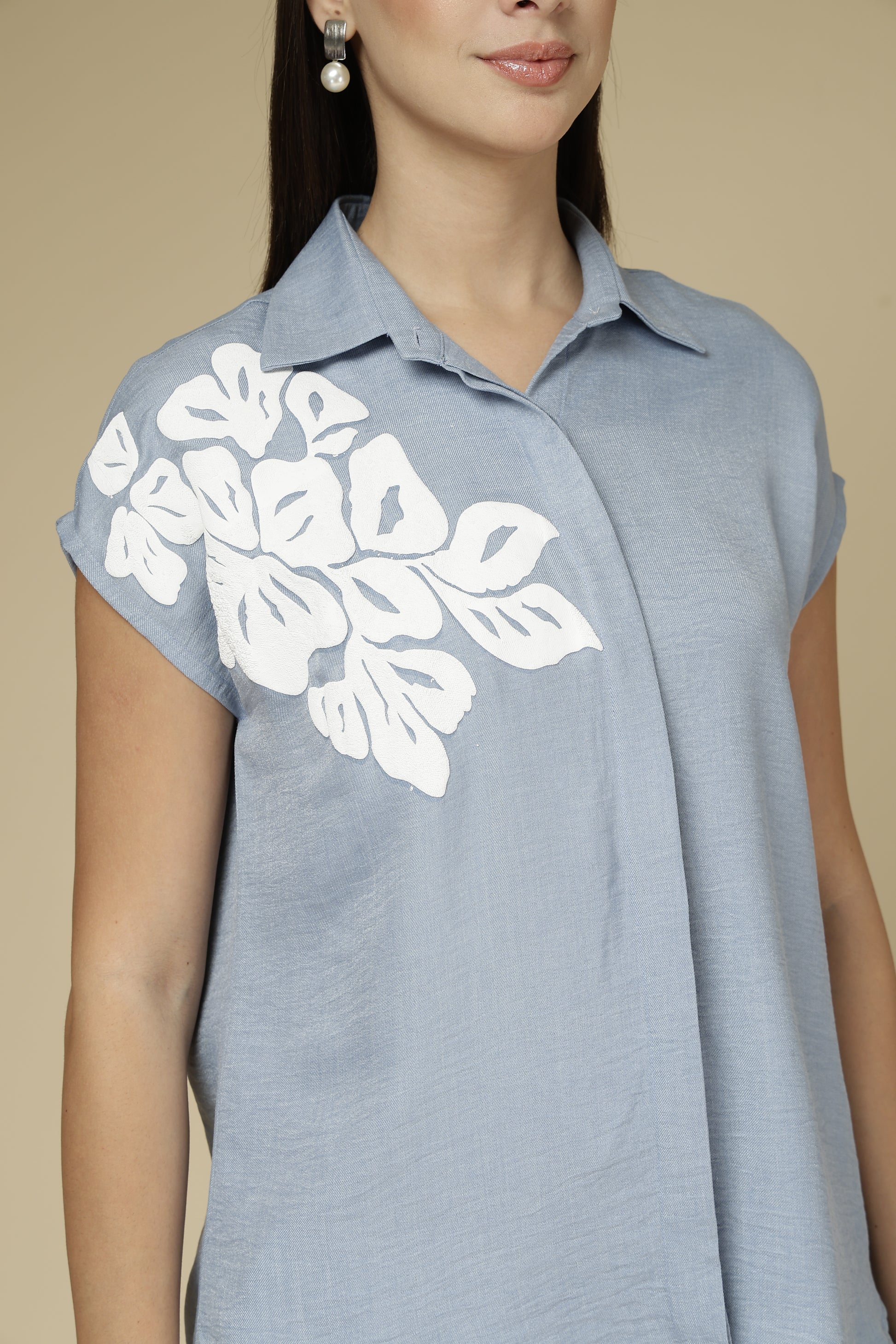 Woman wearing a light blue sleeveless top with white floral patterns on a beige background