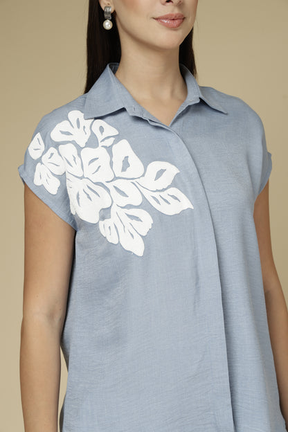Woman wearing a light blue sleeveless top with white floral patterns on a beige background