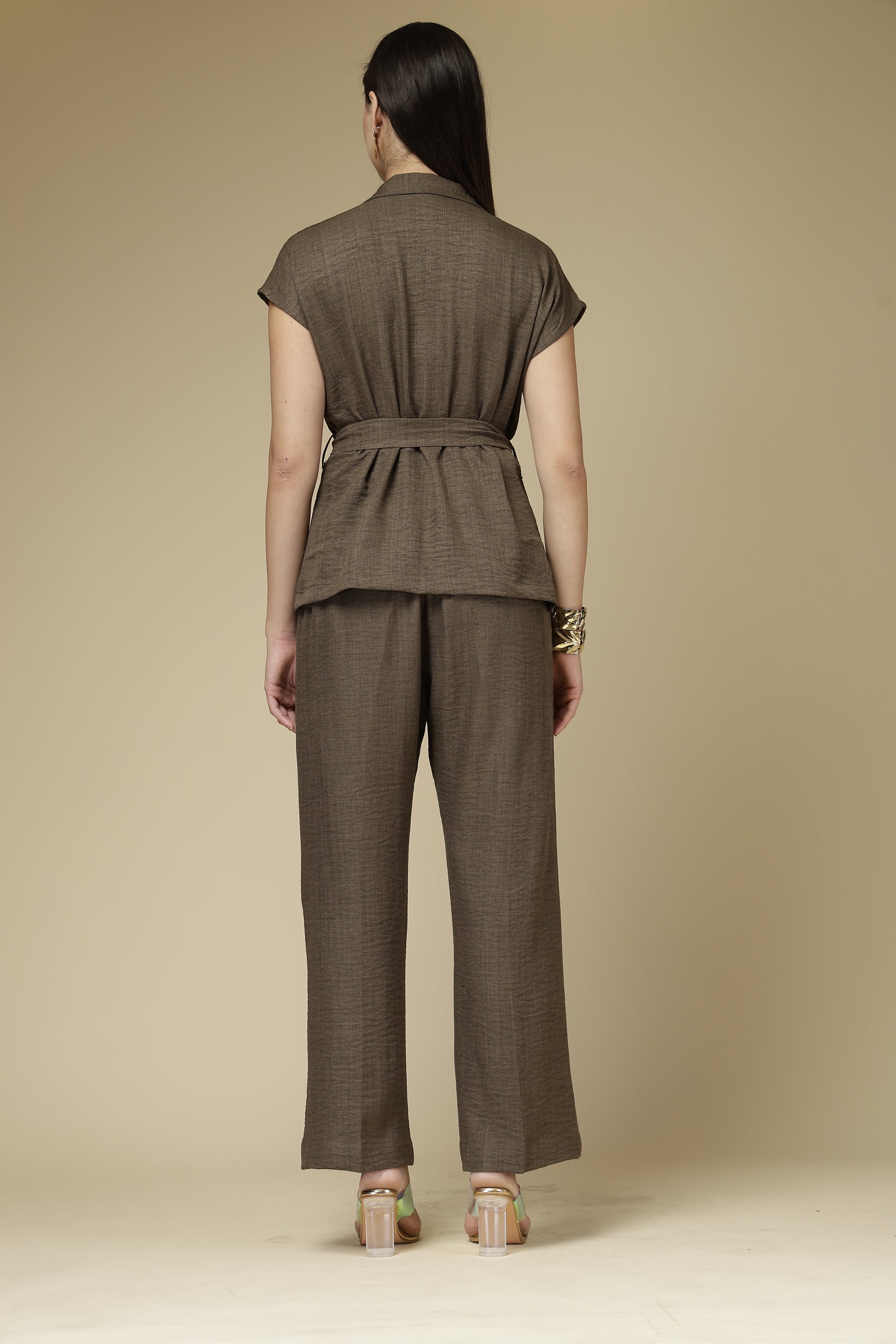 Woman wearing a brown outfit with a belt against a beige background